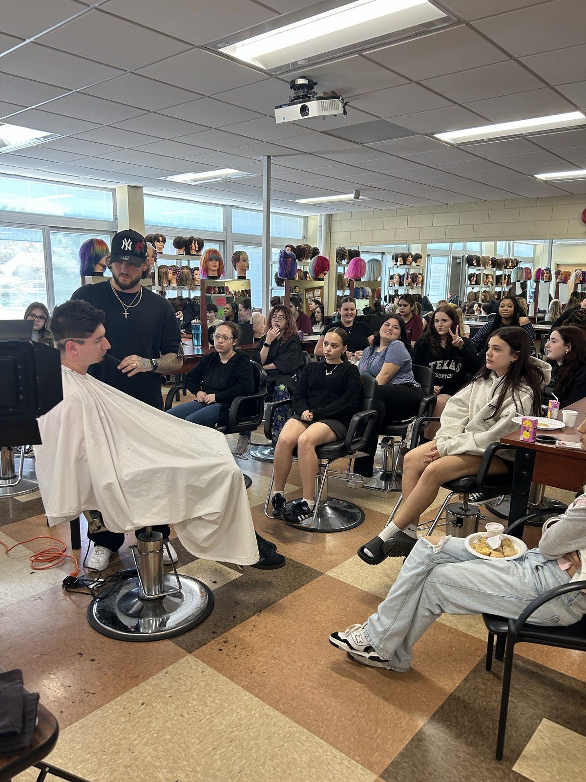 Joey DeCollibus teaching a barbering class, cutting in front of a room of students.